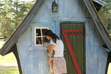 A family (mother and daughter) looking together thorough a fairy-tale house` 's window in the forest