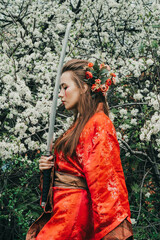 Young girl in traditional kimano in a blooming garden with samurai japanese sword katana in image of warrior woman