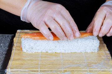The cook puts red salmon fish on the finished sushi roll.