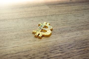 One single golden bitcoin cryptocurrency symbol laying on a wooden desk