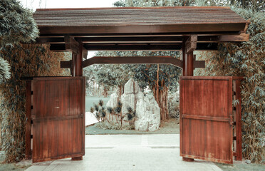 Wooden gates in Japanese style leading to beautiful park with dense vegetation and stone pieces