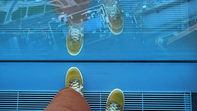 Top view on man's feet in yellow leather sneakers. Man stands near panoramic window on high floor of building. Urban fashion of millennials.