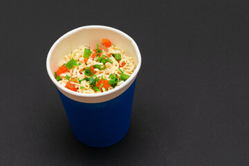Prepared Instant Noodles with Carrot and Greens in Blue Cup on Black Background. Quick Lunch or Unhealthy Fast Food