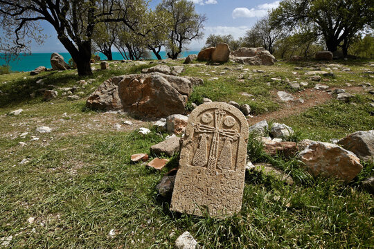 An old Armenian khachkar (hand-carved cross stone) rests on the grass behind the historic Church of the Holy Cross on Akdamar Island in Lake Van, Eastern Anatolia, Turkey