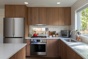 Modern kitchen with oven, gas stove and fridge with brown cabinets and recessed lighting