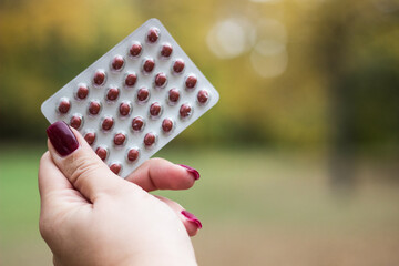 Woman's hand holding blister packs, nature bokeh background