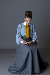 A working class Edwardian woman wearing a striped blouse, mustard yellow cravat, and walking skirt...