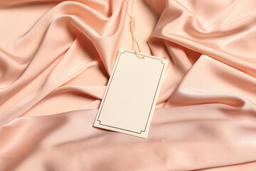 Blank white tag on light pink silky fabric. Space for text