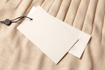 Blank white tags on beige sweater, top view. Space for text