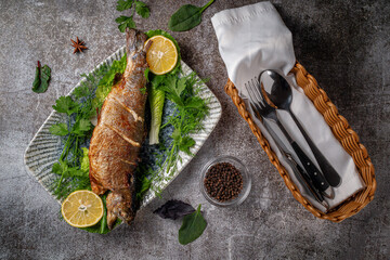 Roasted Whole Trout with lemon, lettuce and dill and parsley greens on a plate against a gray stone table