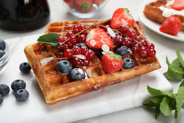 Board with delicious Belgian waffles, berries and caramel sauce on table, closeup