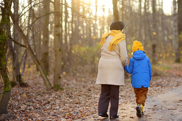 Obraz premium Little grandson and elderly grandmother during walking in autumn park. Friendship granny and grandchild.