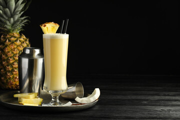 Tasty Pina Colada cocktail and ingredients on black wooden table, space for text