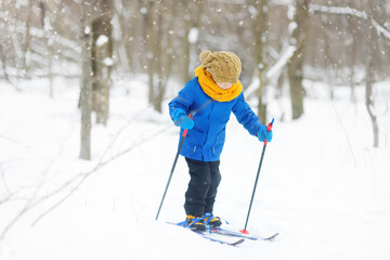 Fototapeta na wymiar Cute little boy is learning ski during walk in the winter forest. Outdoor activities for children in winter. Kids equipment for winter sports.