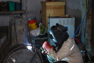 professional welder is welding metal frame and bright sparks in a workshop