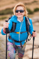 Hiking girl with poles and backpack standing on rocks. Windy autumn day. Travel and healthy...