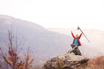 Hiker girl sitting on a rock in the mountains. Enjoying the view with hands up holding hiking...