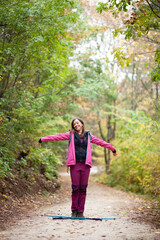 Hiker girl standing on a wide trail in the mountains. Backpacker with pink jacket in a forest. Healthy fitness lifestyle outdoors.