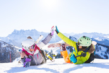 two female friends with ski and snowboard equipment having fun and high five with snow in the air