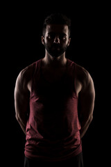 Fototapeta na wymiar Side lit muscular Caucasian man silhouette. Athlete in red shirt posing against black background.