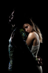 Couple posing on black background. Girl hugging boy in shadow from behind.