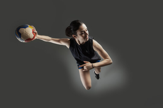 Handball player posing on gray background. Girl jumping with ball.