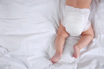 Top view of cute baby in dry soft diaper on white bed. Space for text