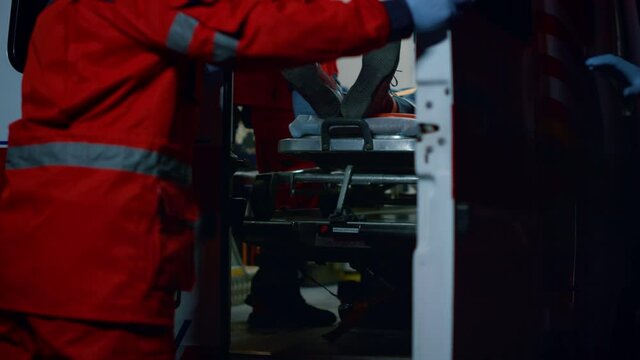 Paramedics transferring man in ambulance. Assistants moving patient to hospital
