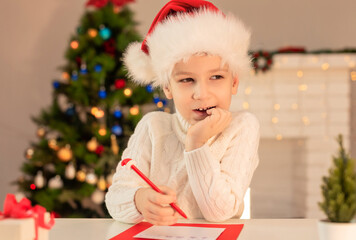 Child boy in red Santa hat writing a letter to Santa Claus. Christmas or New Year cozy holidays concept. Xmas time. Selective focus