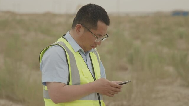 Asian male botanist using his phone to monitor plants during field work in the desert.