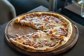 Close up on pizza on the wooden board on the table one piece missing