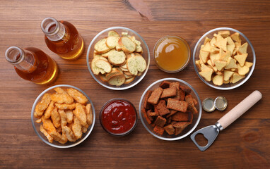 Different crispy rusks, beer and dip sauces on wooden table, flat lay