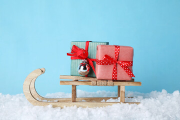 Wooden sleigh with gift boxes, Christmas bauble and artificial snow on light blue background