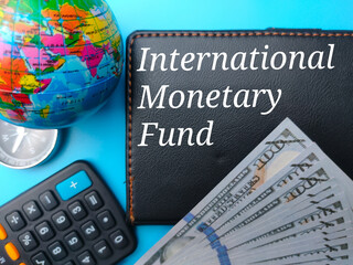 World globe,calculator,banknotes,compass and notebook with text International Monetary Fund on blue background.