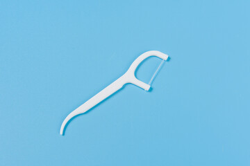 Plastic white dental toothpick with dental floss on blue background.