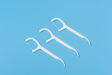 Plastic white dental toothpick with dental floss on blue background.