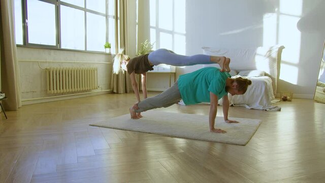 Young couple practicing acro-yoga at home on the floor.