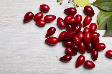 Pile of fresh ripe dogwood berries and green leaves on white wooden table, flat lay. Space for text