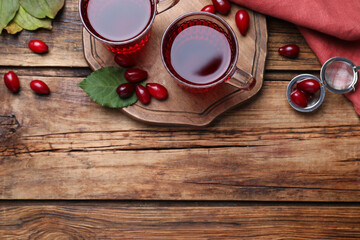 Glass cups of fresh dogwood tea, berries and leaves on wooden table, flat lay. Space for text