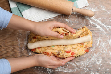 Woman putting marzipan into raw dough for Stollen at wooden table, top view. Baking traditional German Christmas bread