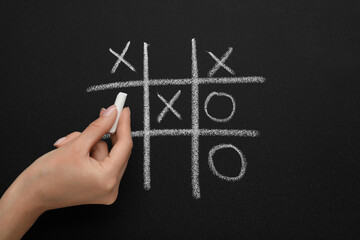 Woman playing tic tac toe game on blackboard, top view