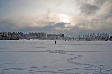 Fototapeta na wymiar A lonely fisherman stands on a frozen pond