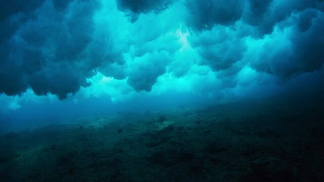 Ocean wave forms underwater clouds. Crystal clear ocean wave rolls and breaks. Underwater view of the powerful ocean wave breaking and creating bubbles
