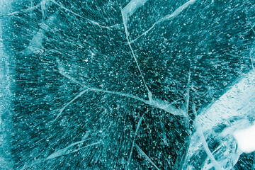 Texture of beautiful blue ice with cracks and air bubbles in the frozen lake. Winter nature background.