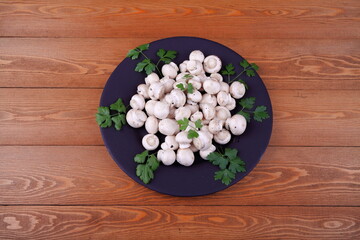 Obraz na płótnie Canvas Fresh Mushrooms and champignons. Laid out on a round black plate. For table setting. On a wooden background. Top view. Close-up. A sprig of greenery.