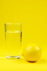 Water in glass and lemon against yellow background Vertical