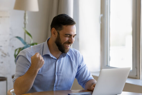 Overjoyed laughing young man looking at computer screen, celebrating getting email with amazing good news, reading online lottery gambling giveaway win notification, making successful profitable deal.