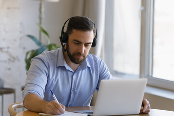 Focused young man in headset with microphone listening educational lecture on computer, studying on...