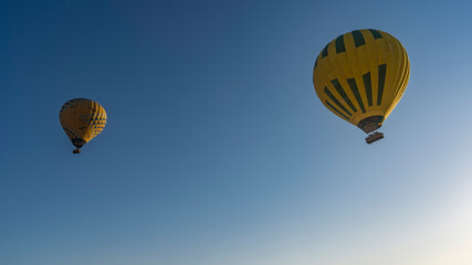 Bright yellow balloons soar in the blue sky. Baskets with tiny silhouettes of people in them are visible. Egypt