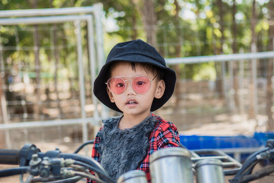 Close up of a boy wearing  hat and fashion glasses.He riding a quad bike on the farm is in a good mood.